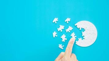 Close up hand holding and playing jigsaw game incomplete. White part of jigsaw puzzle pieces on blue background. concepts of problem solving, business, teamwork, Texture photo with copy space for text