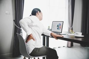 Young asian woman is sitting at work and has tension pain in her neck. Concept office syndrome backache pain from occupational disease, Female having muscle pain from using laptop computer, back pain. photo