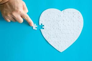 Close up hand holding and playing jigsaw game incomplete. White part of jigsaw puzzle pieces on blue background. concepts of problem solving, business, teamwork, Texture photo with copy space for text