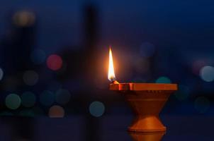 Selective focus on flame of clay diya lamp with colorful city bokeh lights. Diwali festival concept. photo