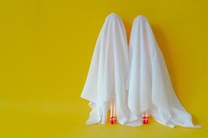 Two girl dolls cover with white sheet costume on yellow background. Minimal Halloween scary concept. photo