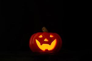 Halloween jack-o-lantern with yellow light from candle in dark background. photo