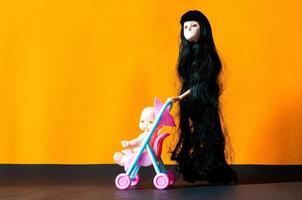 Long hair female flying ghost doll with her baby in a stroller on orange and black background. Minimal Halloween scary concept. photo