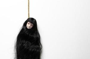 Long hair asian female ghost doll hanging with the rope acting commit suicide on white background. Minimal Halloween scary concept. photo