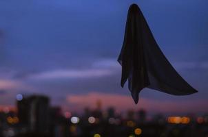 Ghost sheet flying in dusk sky with city lights background. Halloween scary concept. photo