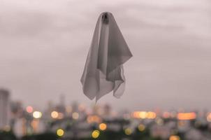 White ghost sheet flying in dusk sky with city lights background. Halloween scary concept. photo