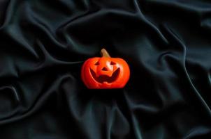 Halloween pumpkin on black satin fabric background. Halloween minimal concept. photo