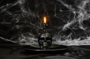 Scary halloween dinner party concept with skull candle puts on black plate that have cobweb on black background. photo