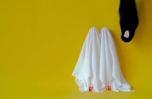 Two girl dolls cover with white sheet costume with female ghost head with long hair hanging from the top on yellow background. Minimal Halloween scary concept. photo