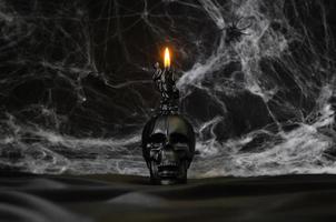 Scary halloween background with skull that have candle on top puts on black satin fabric with cobweb. photo