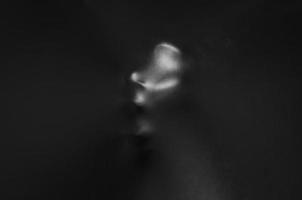 cara humana gritando presionando a través de tela negra con brillo y lado oscuro para el concepto de fondo de halloween. foto