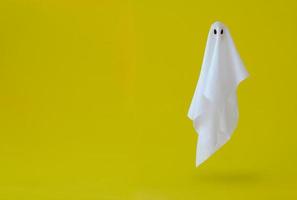 White ghost sheet costume flying in the air with yellow background. Minimal Halloween scary concept. photo
