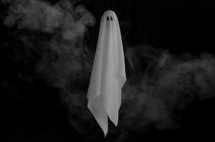 White ghost sheet flying in dark background with smoke. Halloween scary concept. photo