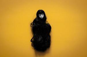 Long hair smiling female ghost doll on yellow background. Minimal Halloween scary concept. photo