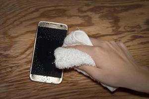 Hands holding White cloth with wet smartphone drops on wooden floor photo