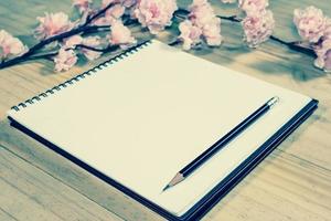 open note book with pink sakura flowers on wooden background,filter effect. photo