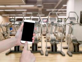 hand holding mobile smart phone with blur fitness gym equipment background,Vintage filter photo