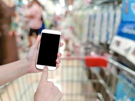 hand holding mobile smart phone with blur shelves in supermarket background photo