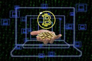 Human hand holding piles of coins with bitcoin symbol and laptop icons on binary background photo
