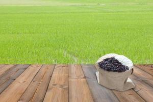 Wooden table and Jasmine rice with green paddy rice field background photo