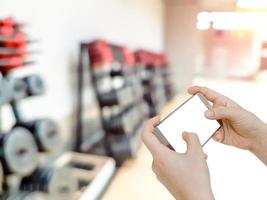 hand holding mobile smart phone with blur fitness gym equipment background photo