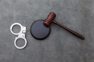 Law theme. Court of law trial in session. Judge gavel handcuffs on grey table in lawyer office or court session. Mallet of judge on concrete stone grey background. Justice human rights concept. photo