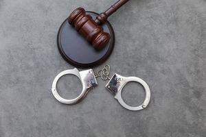 Law theme. Court of law trial in session. Judge gavel handcuffs on grey table in lawyer office or court session. Mallet of judge on concrete stone grey background. Justice human rights concept. photo