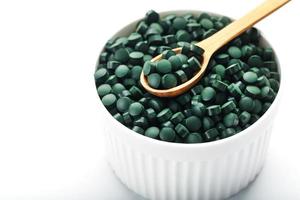 Green tablets made of natural organic spirulina in a cup on a white background with free space photo