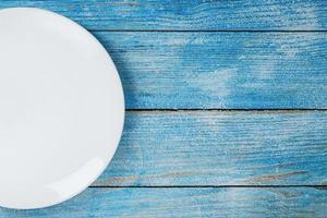 un plato blanco redondo vacío sobre una mesa de madera azul. foto