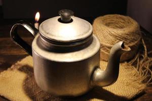 Old old teapot, a vintage metal teapot sits on a wooden table with low light photo