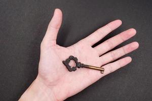 Male hand holding metal key on black background photo