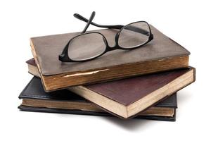 A stack of old books with eyeglasses on a white background. photo