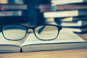 Close up of open book with eyeglasses on wooden desk, Soft focus, Vintage tone photo