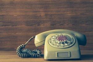 Old telephone on wooden table background. Vintage tone photo