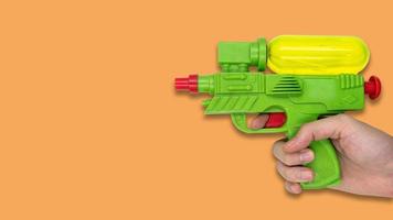Hand holding gun water toy on orange background. Free space for text photo