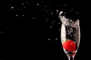 Fresh strawberry with water splash in glass on black background. photo