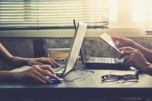 compañeros de trabajo que trabajan en el mismo escritorio, están usando una computadora portátil con tableta, concepto de negocio de inicio, tono vintage foto