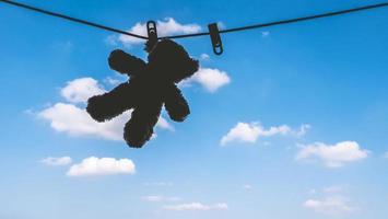 Silhouette of Teddy bear hanging on the clothes line with blue sky. photo