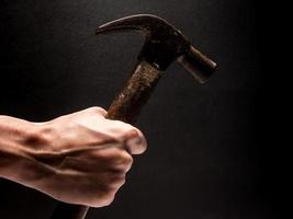 mano masculina sosteniendo un martillo sobre fondo negro. foto