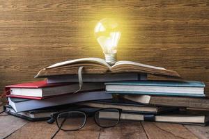 Open book with light bulb, hardback books and glasses on wooden table. photo