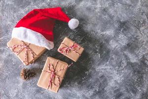 Top view of santa hat with gift packages wrapped in brown paper on gray grunge background. Free space for text photo