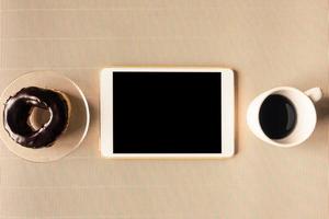 Top view of tablet with coffee cup and donut on table. photo