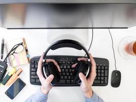 vista superior de las manos masculinas trabajando en la computadora y sosteniendo los auriculares en el escritorio. foto