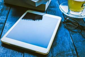 Tablet with glasses,book and tea cup on wooden table photo