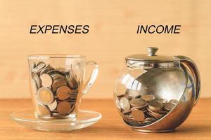 Coins in a cup and a jar on a wooden table, expenses and income text, financial concept photo