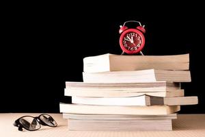 Stack of books with eyeglasses and clock on wooden table, Black background photo