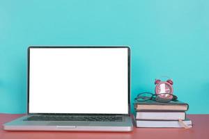 Modern laptop with blank screen, books, glasses and clock on pastel color background. photo