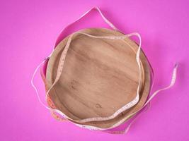 Empty wooden dish with tape measure on pink background. photo
