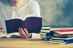 Close up of a man reading a book and making his notes on the wooden table. Vintage tone photo