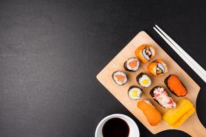 Top view of Sushi set on wooden tray with chopsticks and sauce on black background, Japanese food. Free space for text photo